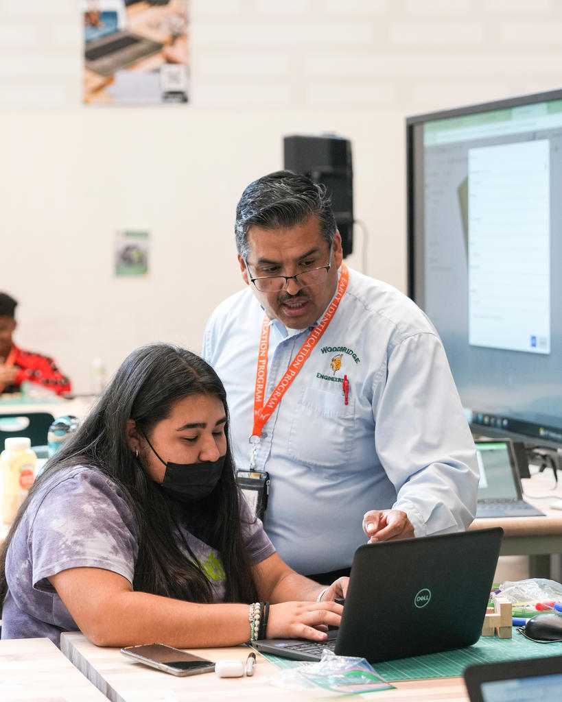 A teacher helps a student figure out a problem on their laptop.